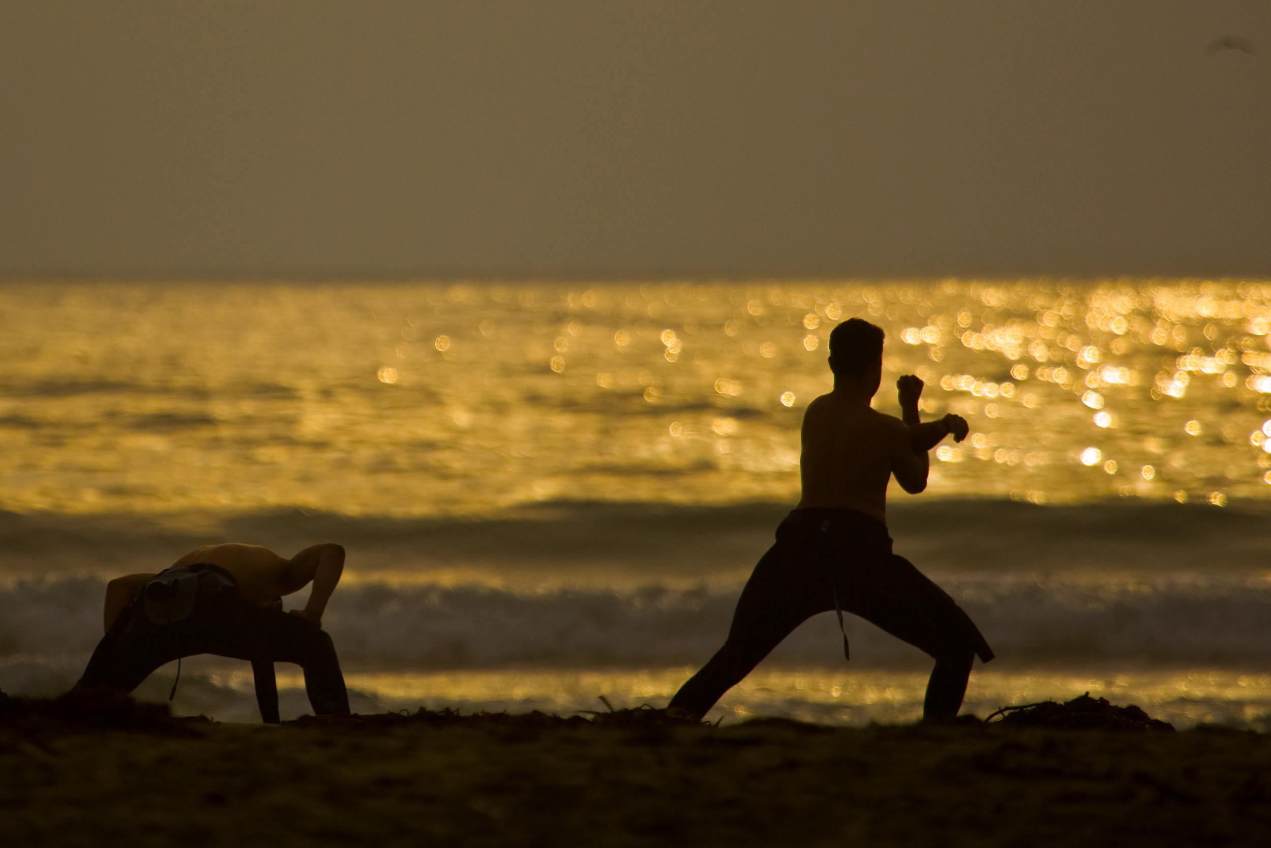 Two Surfers do Pre-stretches on Morro Strand State Beach prior to a sunset surf session